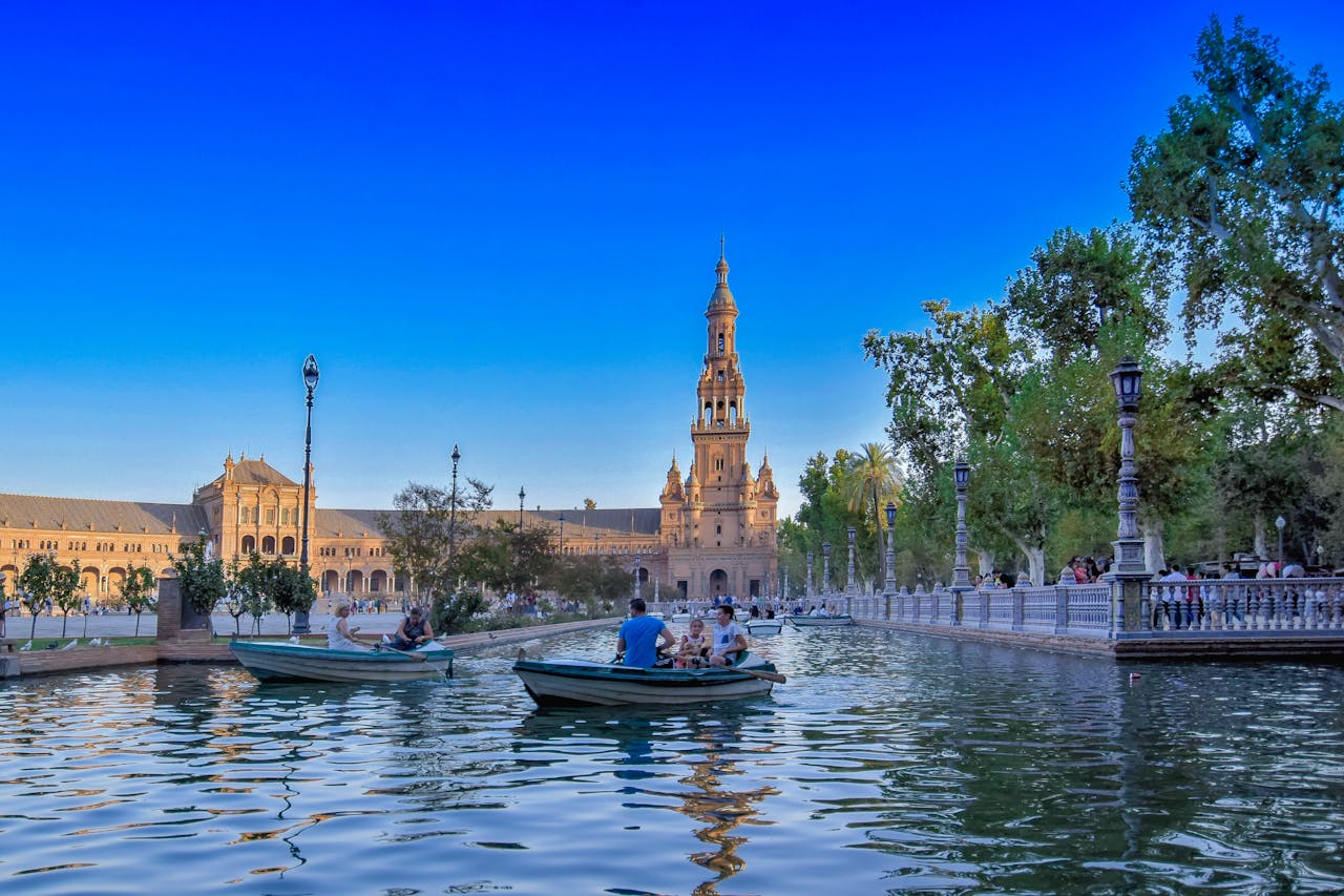 Colorful view of people boating in Plaza de España, Seville under a clear sky.